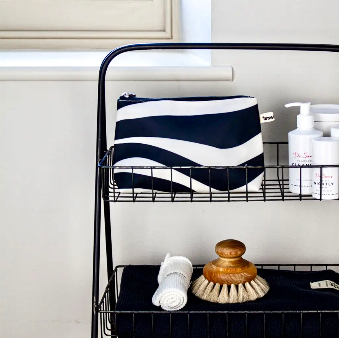 Brownstone London Surf Wide Make Up Bag on a wire shelf with cleaning supplies