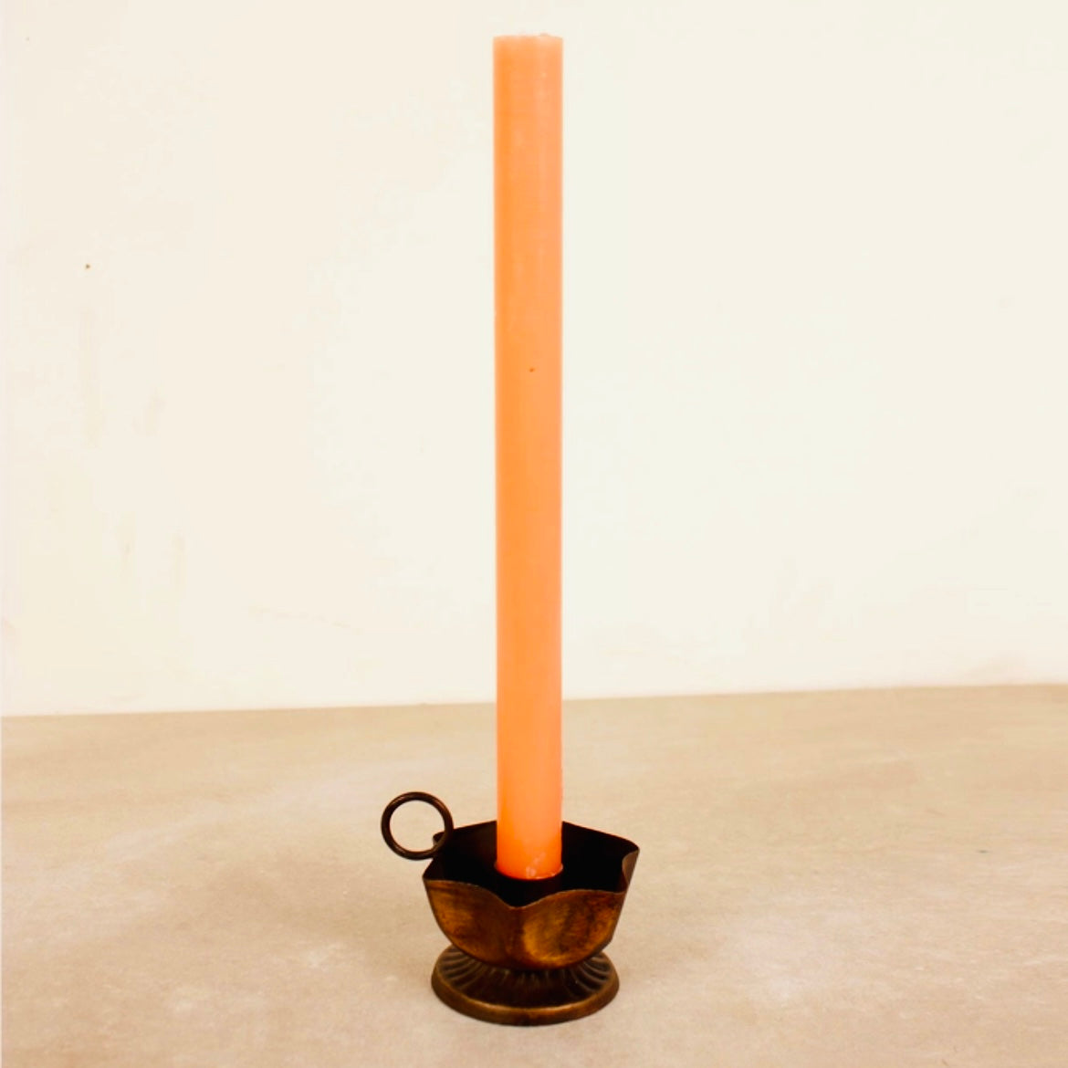Tall peach-colored candle in a decorative Frill Candle Holder on a beige surface with a light beige background