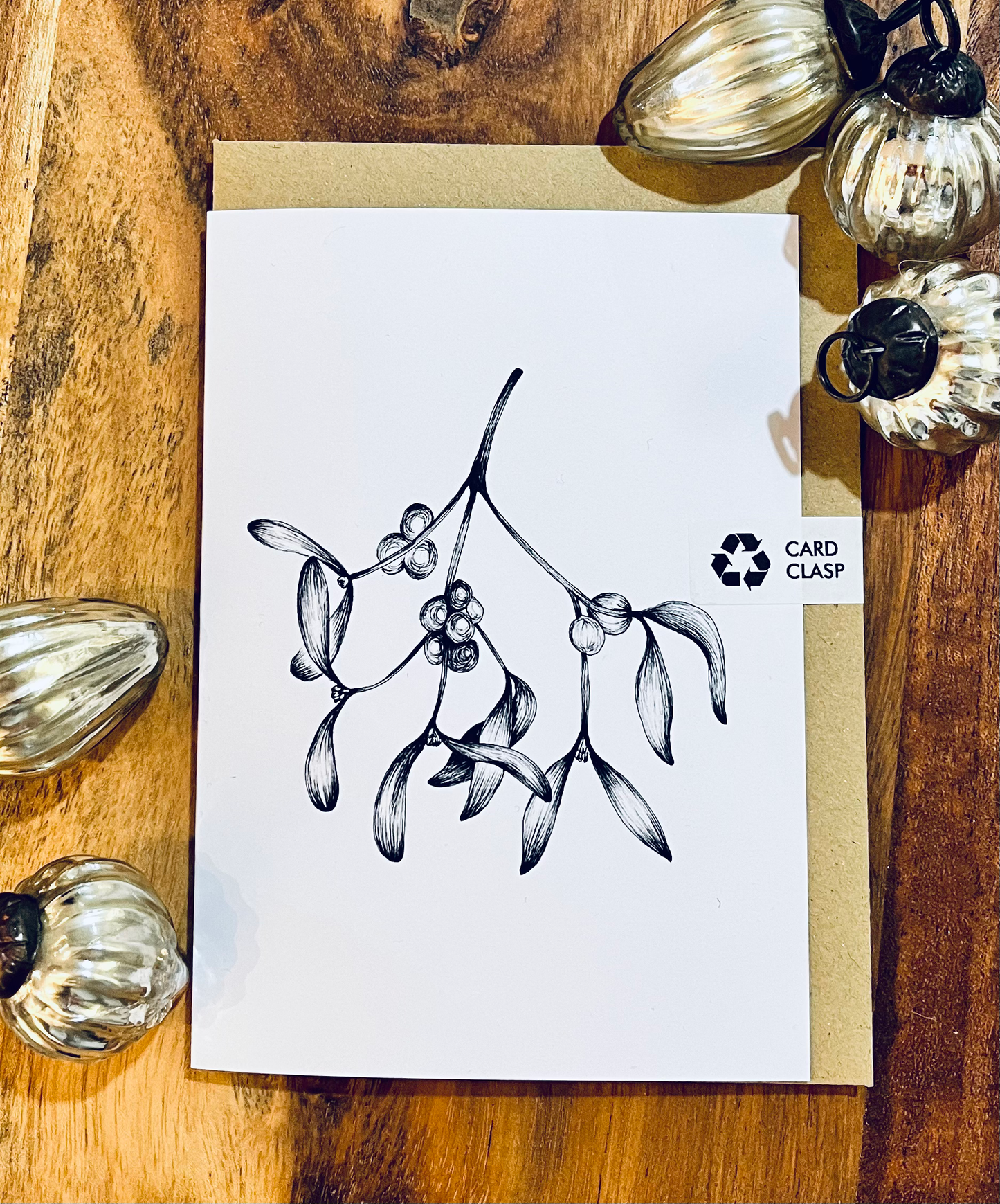 Card with mistletoe design on a wooden surface with decorative pumpkins.