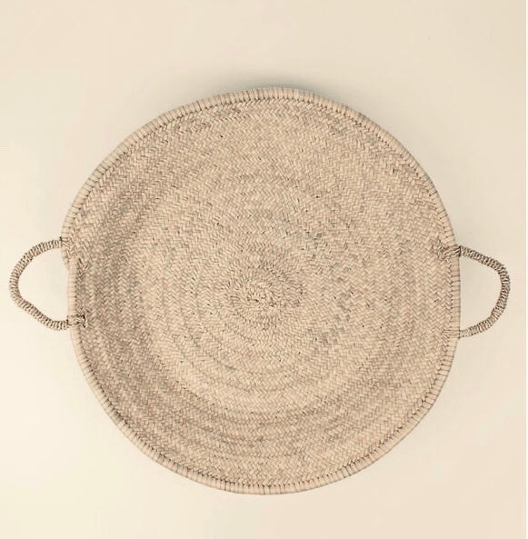 Round woven mat with handles on a beige background