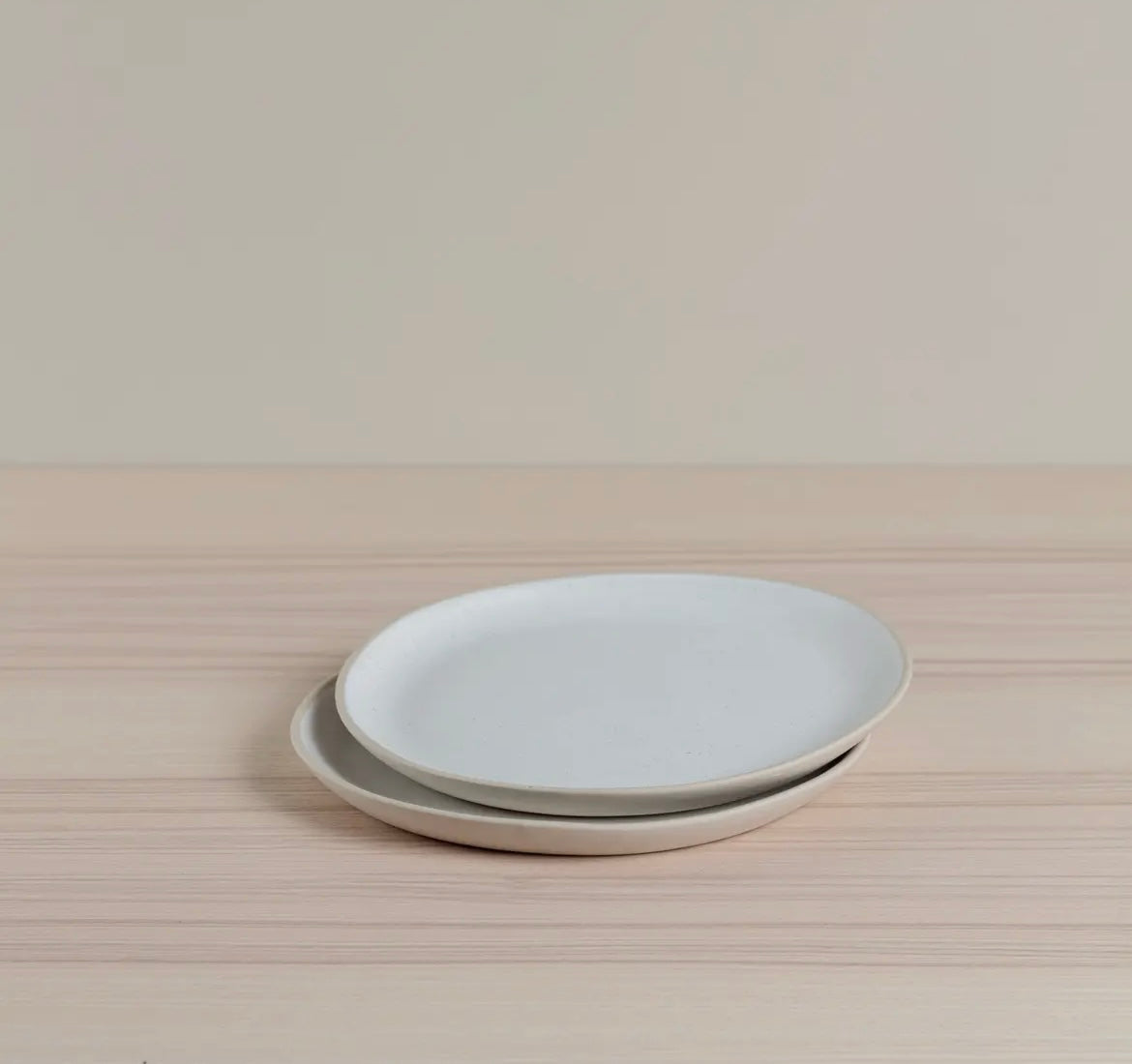 Two light gray Organics Side plates stacked on a wooden surface with a neutral background