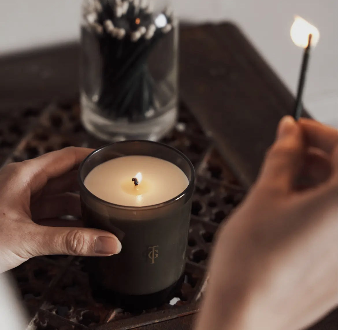 Person holding a lit candle in a black holder with a blurred background