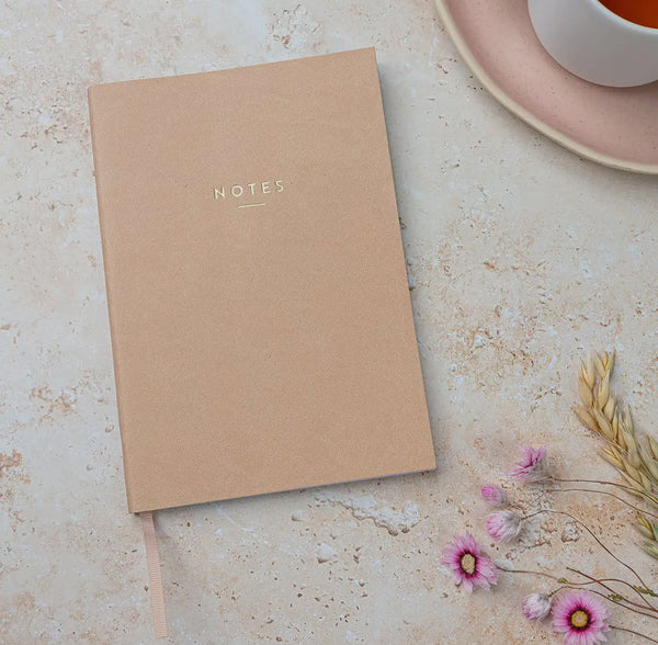Kraft paper notebook labeled 'NOTES' on a light surface with flowers and a cup.