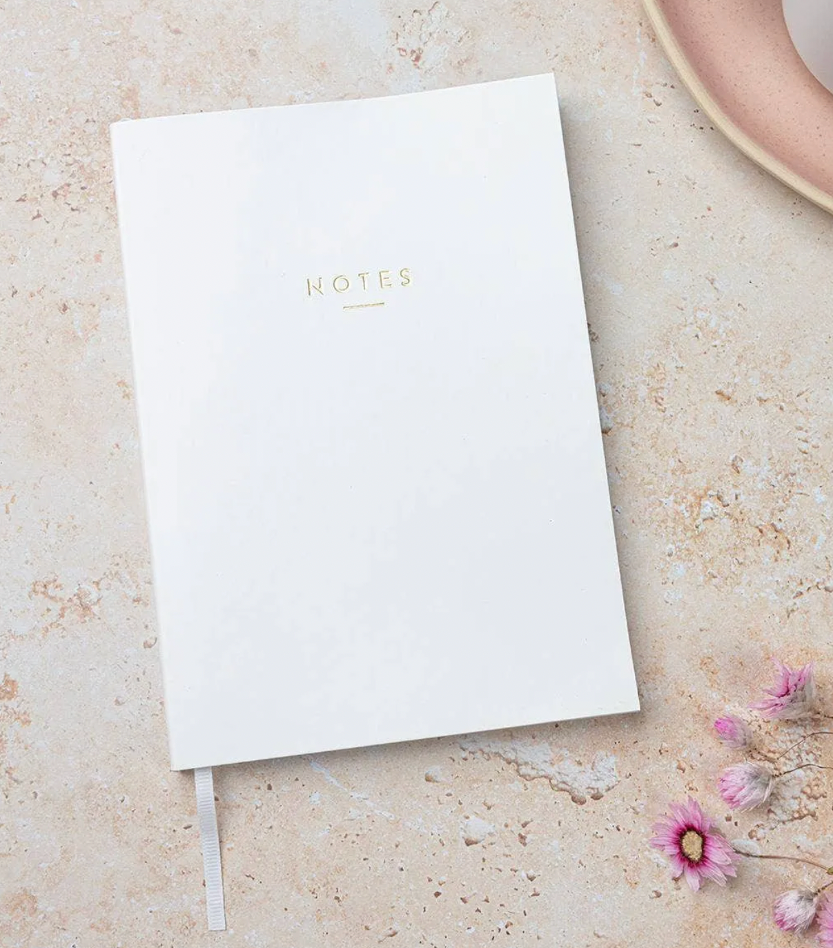 White notebook with 'NOTES' on a beige surface with flowers