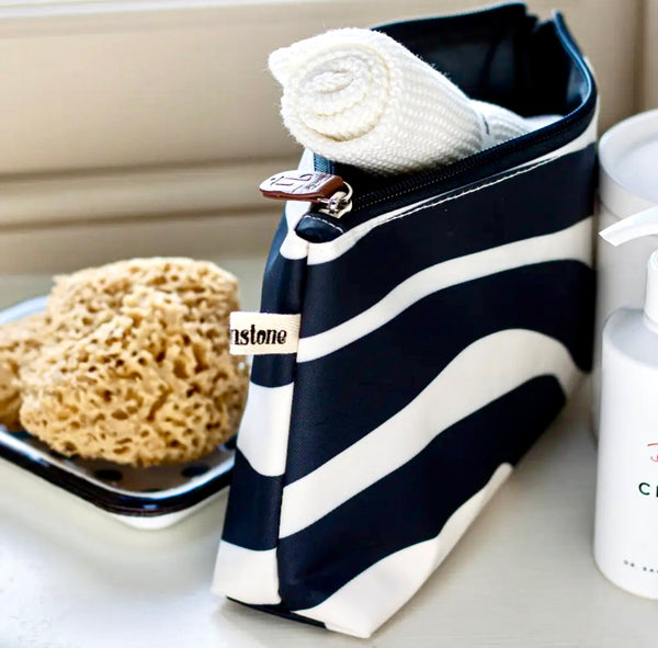 Black and white striped Brownstone London Surf Wide Make Up Bag with a sponge and bottle on a surface