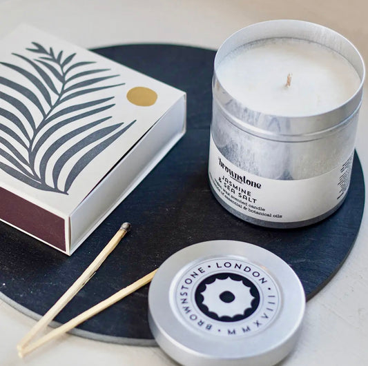 Candle in a tin with packaging and matches on a dark surface