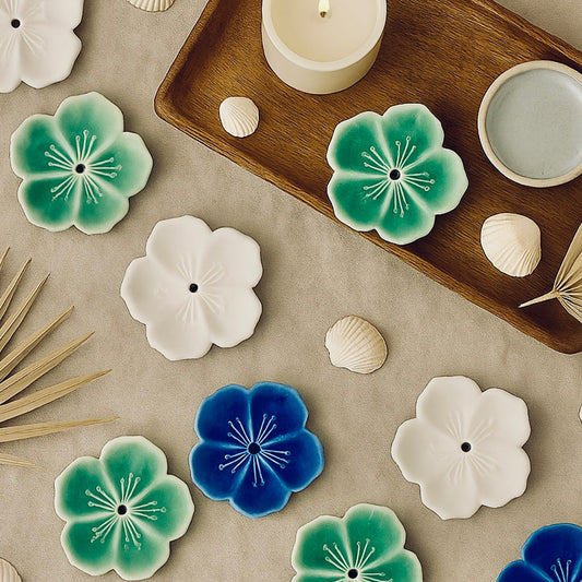 Decorative ceramic flowers on a neutral surface with a wooden tray and candle.