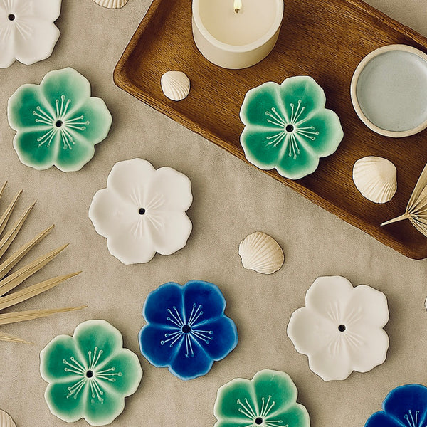 Decorative ceramic flowers on a neutral surface with a wooden tray and candle.