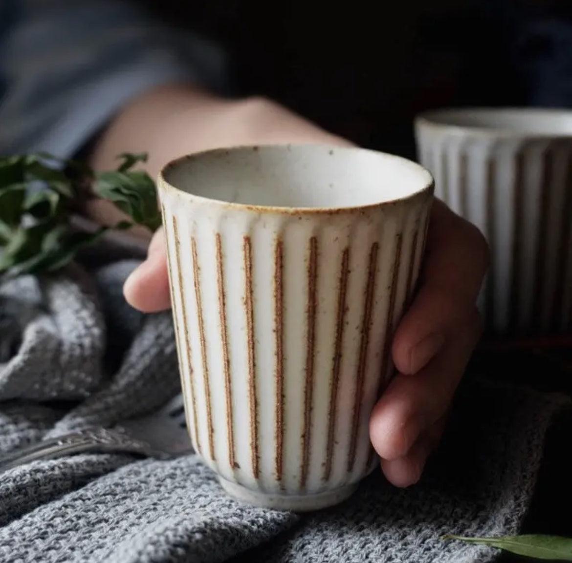 Hand holding a ceramic mug with vertical stripes on a textured surface.