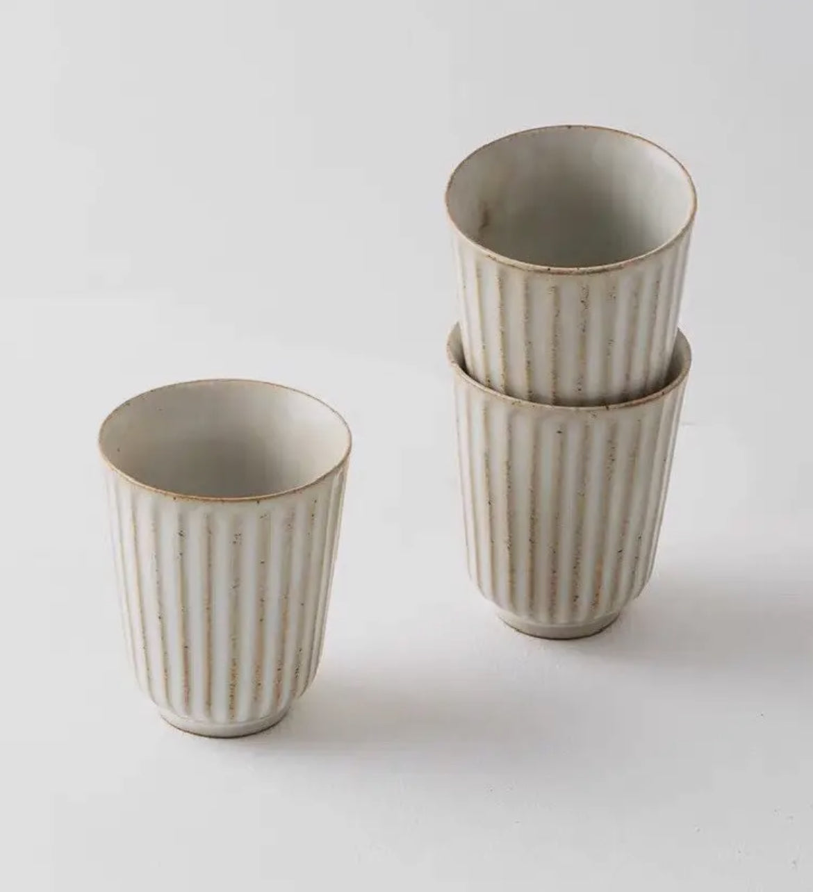 Set of three ceramic cups with ribbed texture on a light gray background
