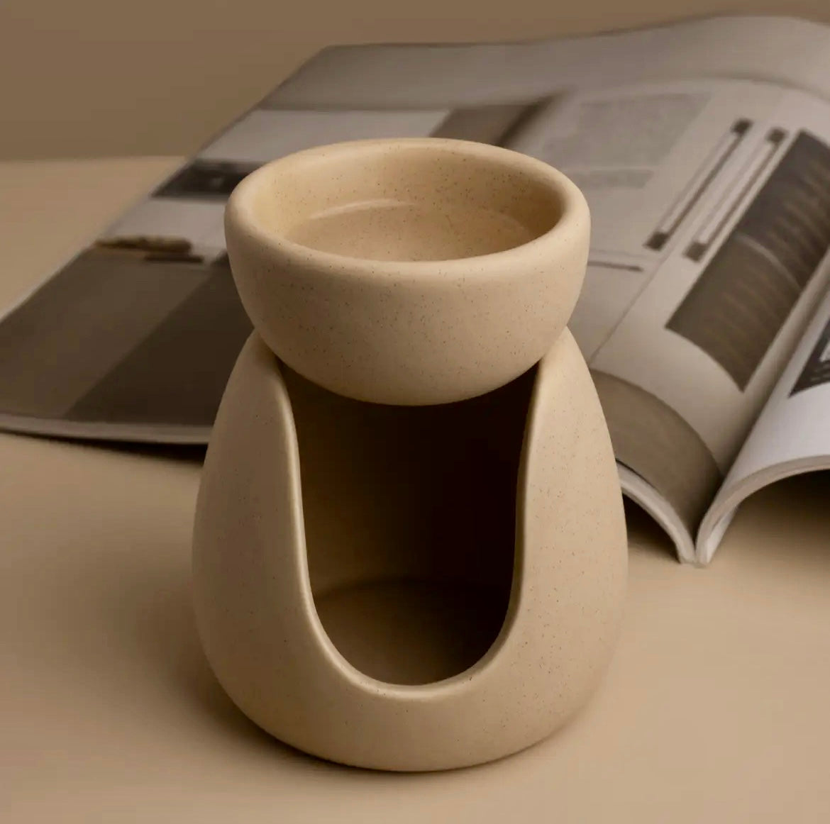 Beige ceramic oil burner on a beige surface with an open magazine in the background
