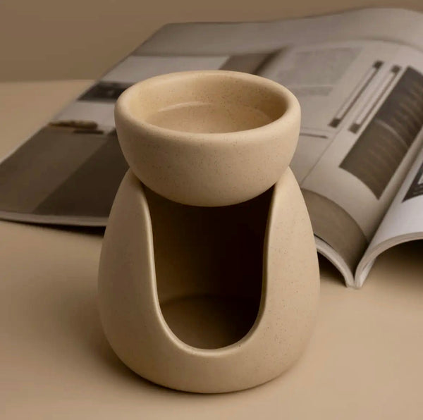 Beige ceramic oil burner on a beige surface with an open magazine in the background