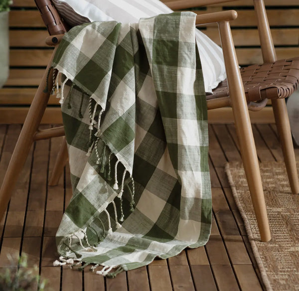 Green and beige checkered blanket draped over a wooden chair on a wooden floor.