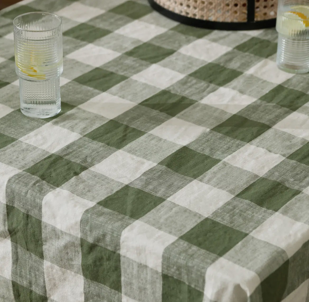 Green and white checkered throw with a glass of water on a table.