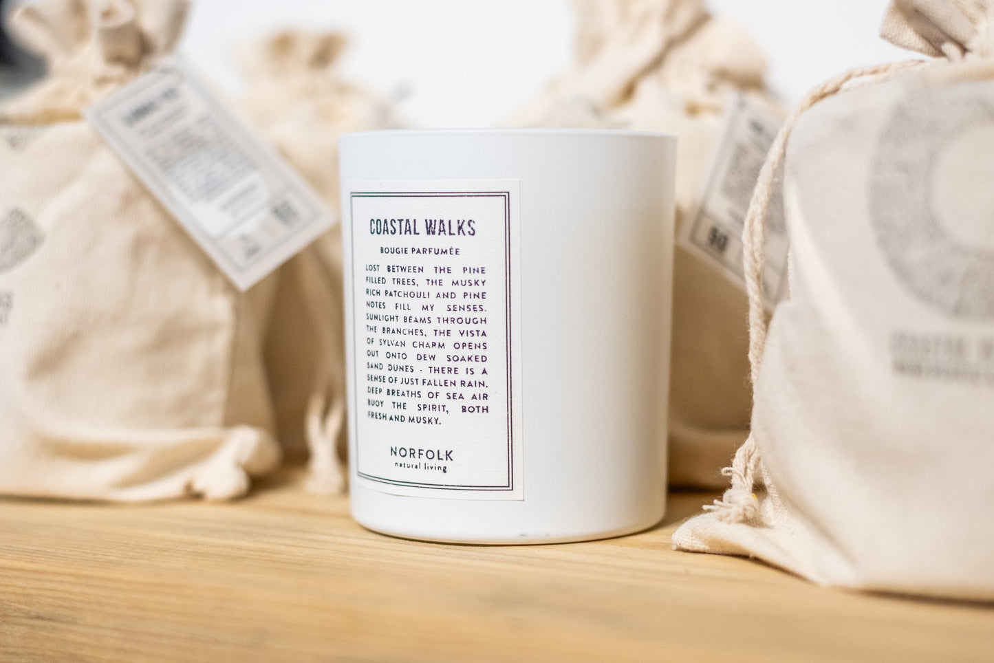 Coastal Walks Candle labeled 'Coastal Walks' with a white label on a wooden surface, surrounded by beige fabric.