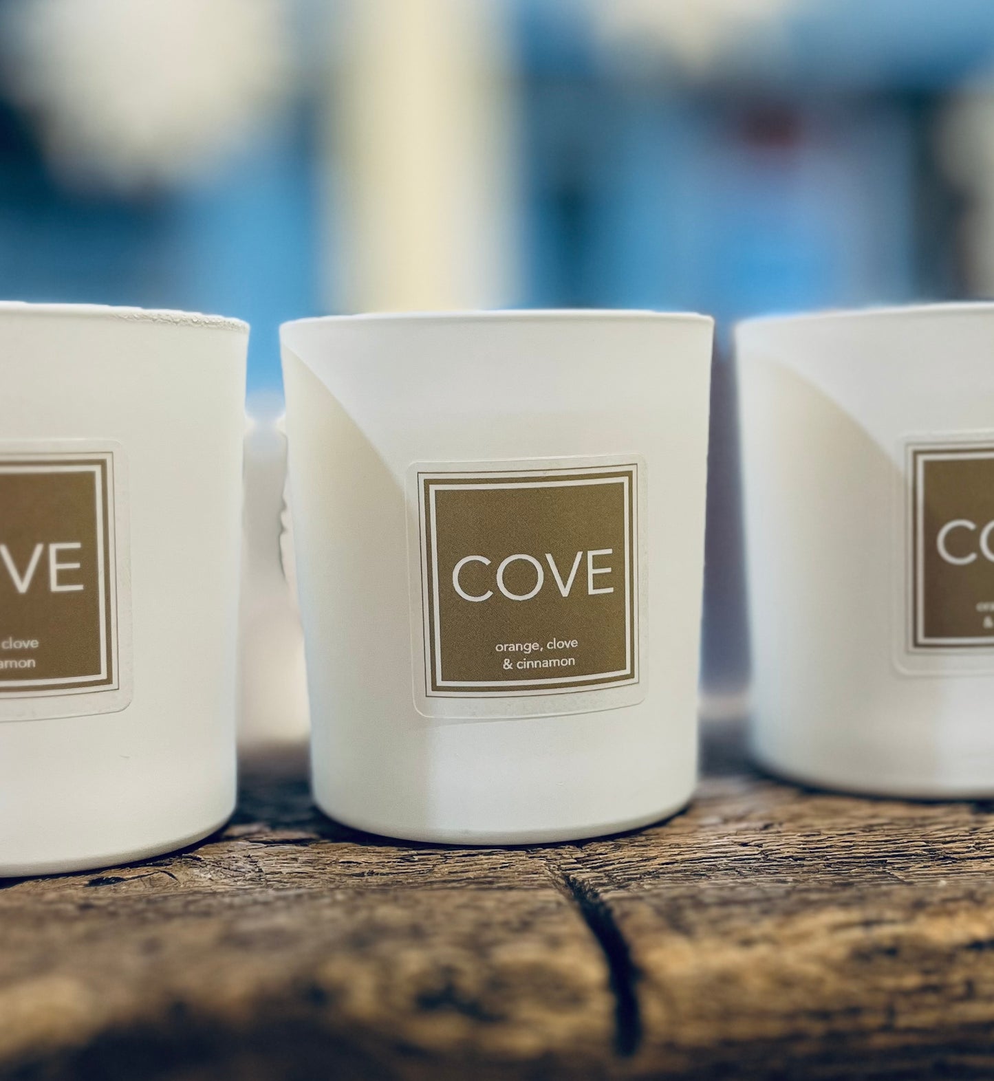 Three white candles with 'Cove' labels on a wooden surface