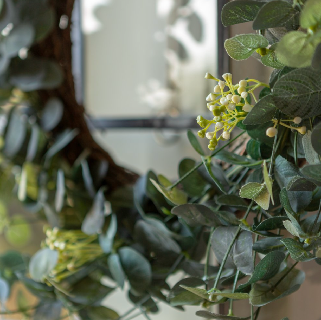 Close-up of a wreath with green leaves and small white flowers, blurred background