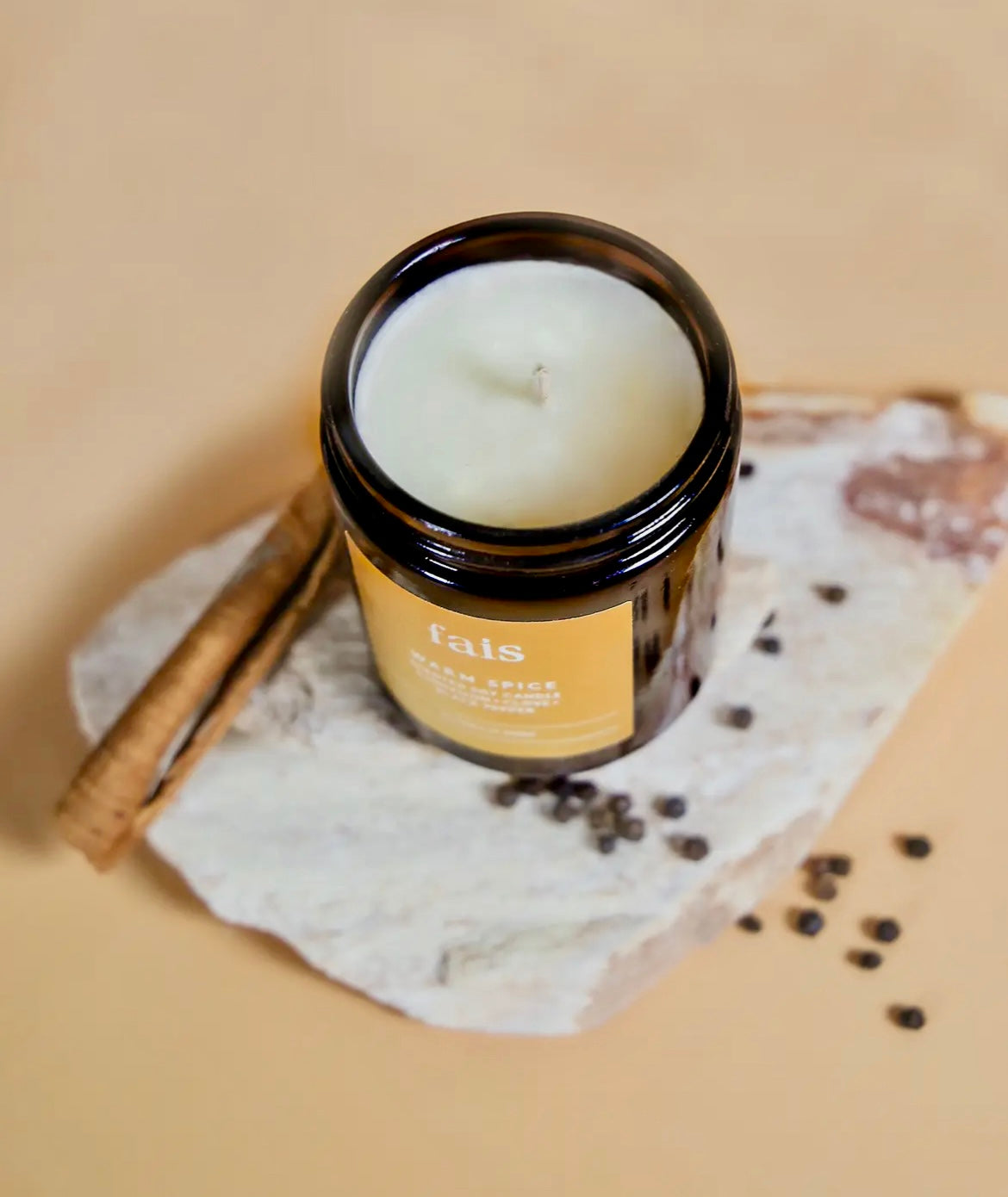 Fais Warm Spice Soy Candle in a glass jar with a label on a stone surface
