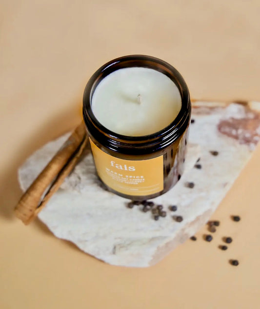 Fais Warm Spice Soy Candle in a glass jar with a label on a stone surface