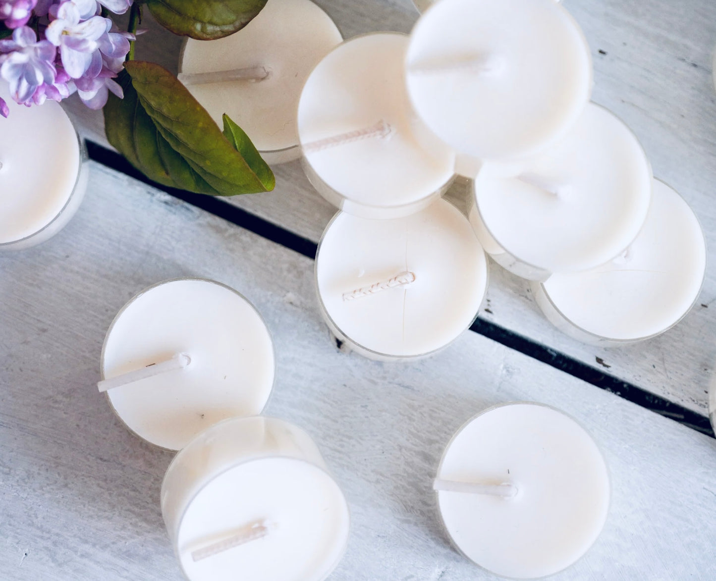 White candles on a light wooden surface with a floral arrangement in the background