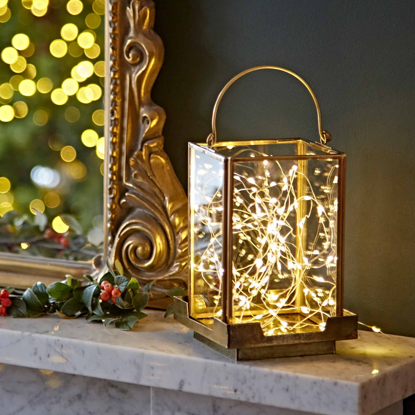 Decorative lantern with string lights on a marble surface with a mirror and festive decorations in the background.