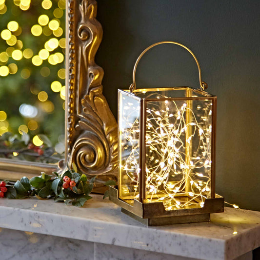 Decorative lantern with string lights on a marble surface with a mirror and festive decorations in the background.