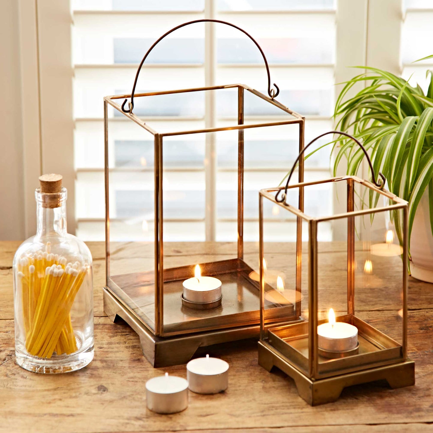 Two gold lanterns with candles on a wooden surface near a window.