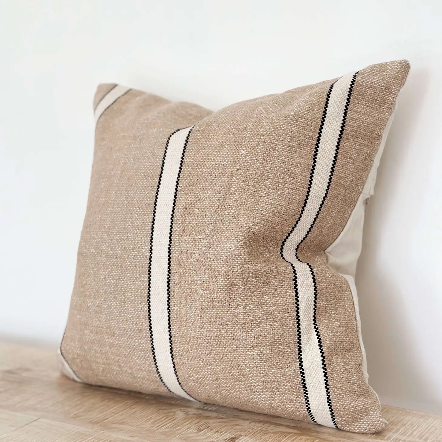Beige pillow with black and white stripes on a wooden surface