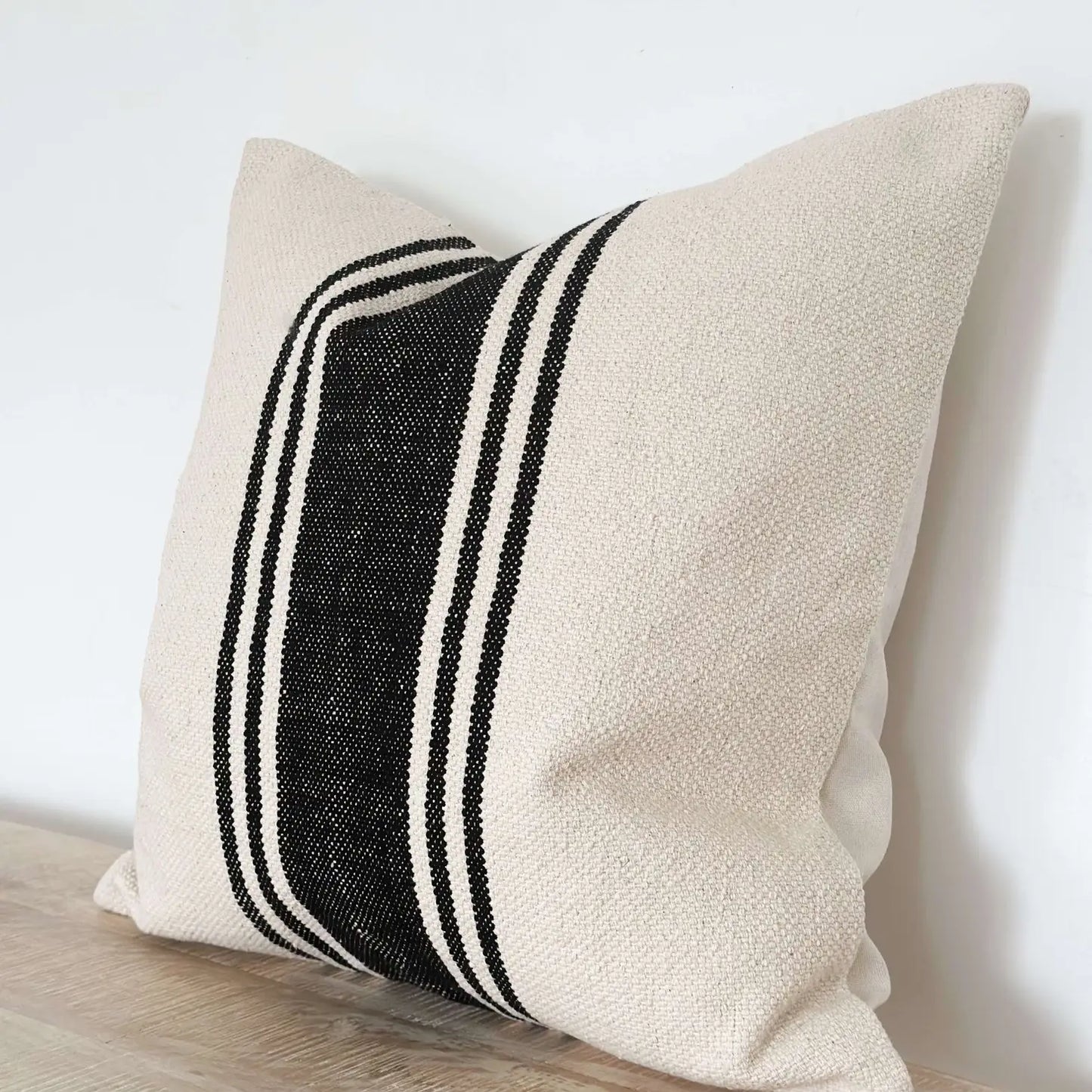 Beige pillow with black stripes on a light wooden surface.