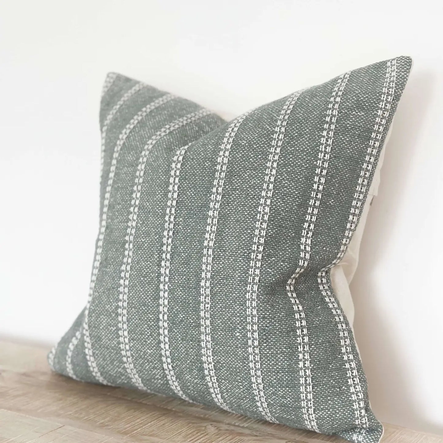Textured green pillow with white stripes on a neutral background