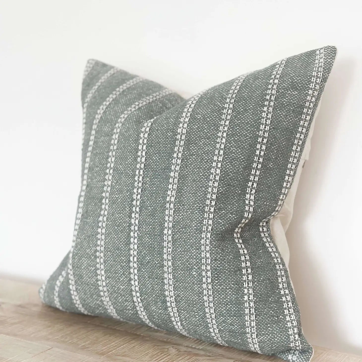 Textured green pillow with white stripes on a neutral background