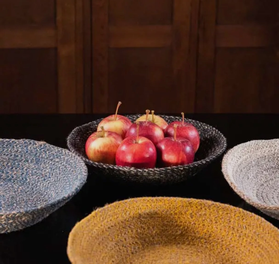 Bowl of apples on a dark surface with woven baskets around
