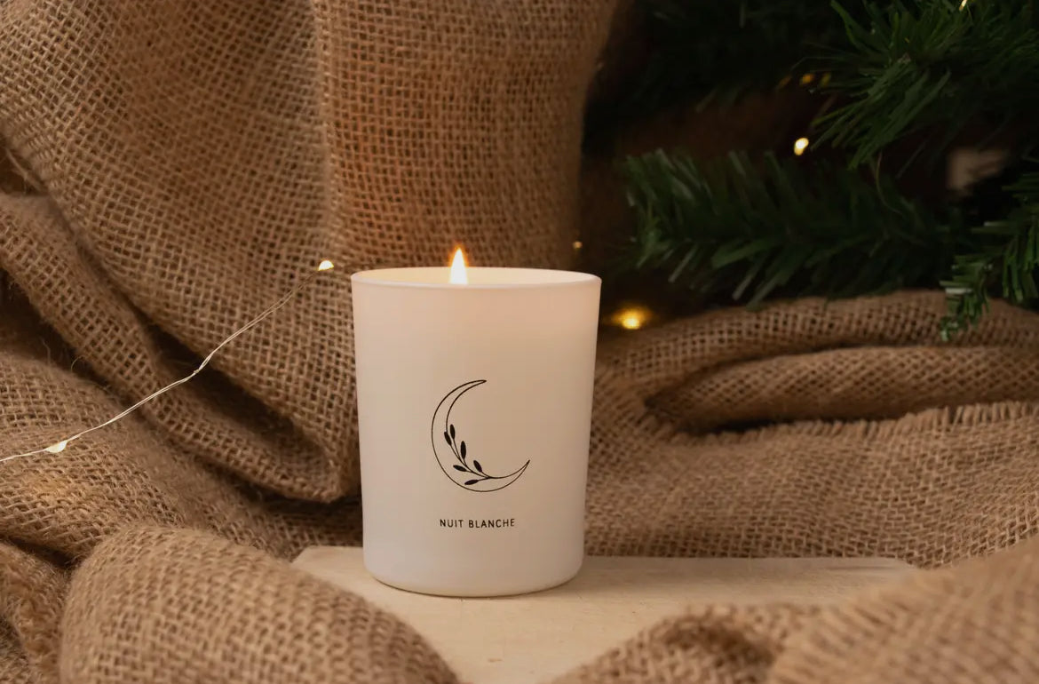 White candle with a logo on a burlap surface with Christmas decorations