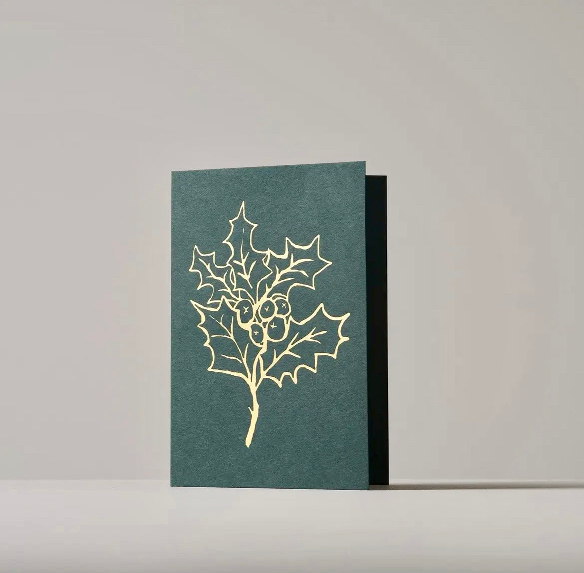 Green card with gold holly leaf design on a gray background