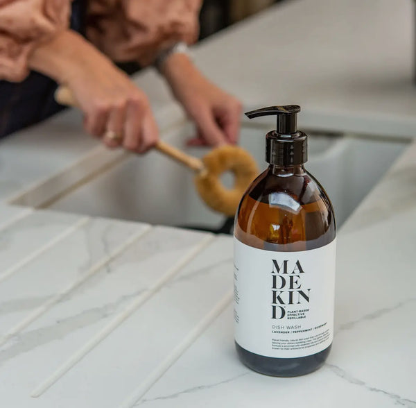 Bottle of 'MADE KIN' product on a kitchen counter with a person cleaning.