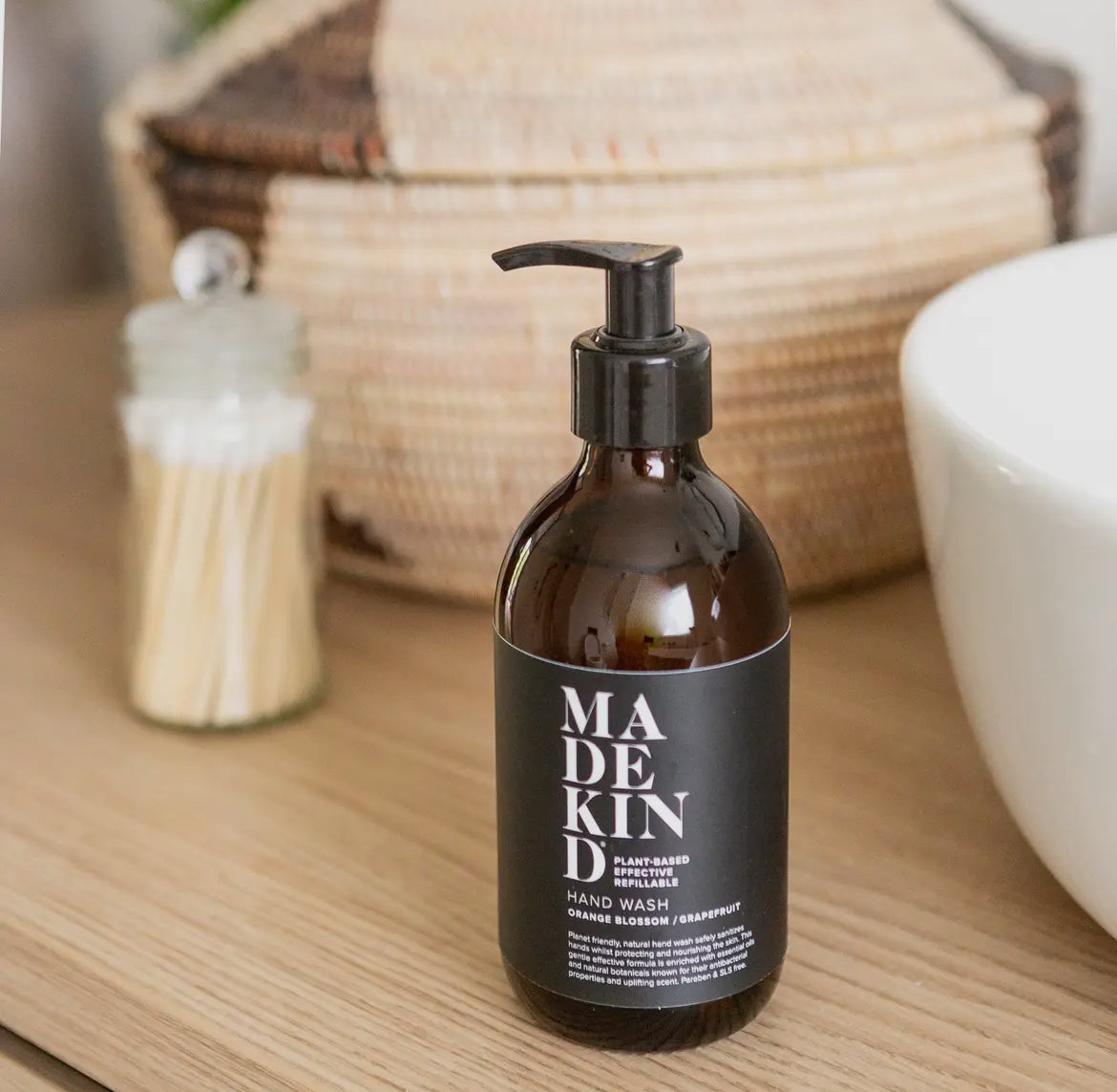 Brown bottle of Madekin hand wash on a wooden surface with a wicker basket and white bowl in the background.