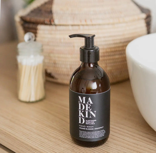 Brown bottle of Madekin hand wash on a wooden surface with a wicker basket and white bowl in the background.