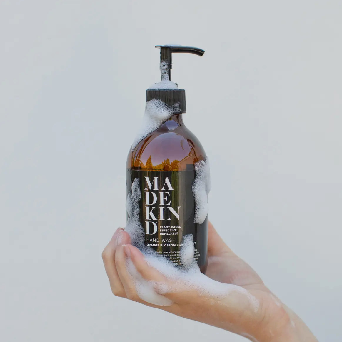 Hand holding a bottle of Madekin hand wash with a light gray background