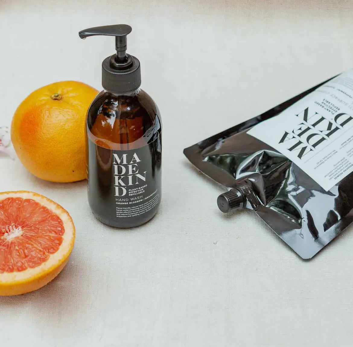 Hand wash bottle with pump, oranges, and a black pouch on a light surface