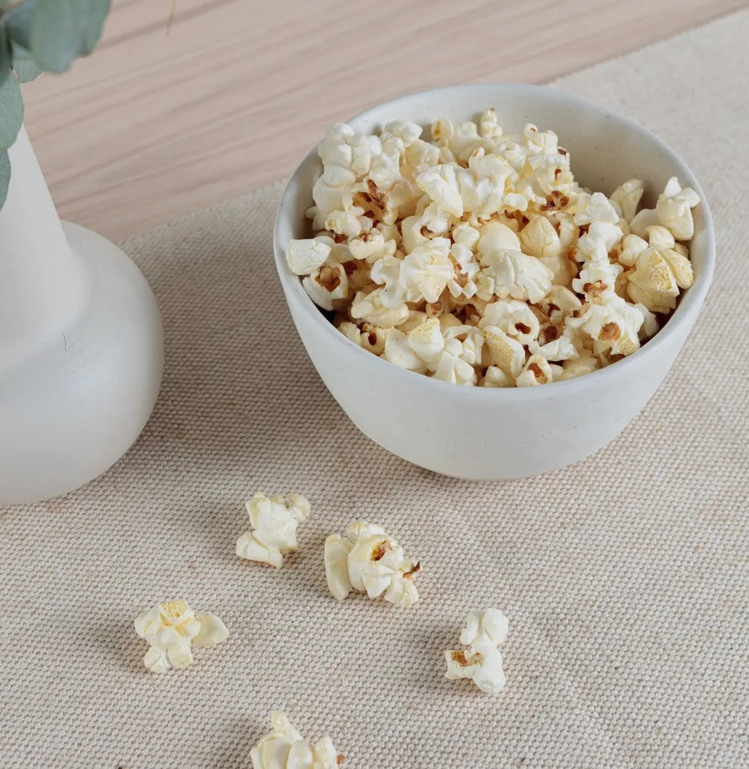 White Organics Nibbles Bowl filled with popcorn on a textured surface