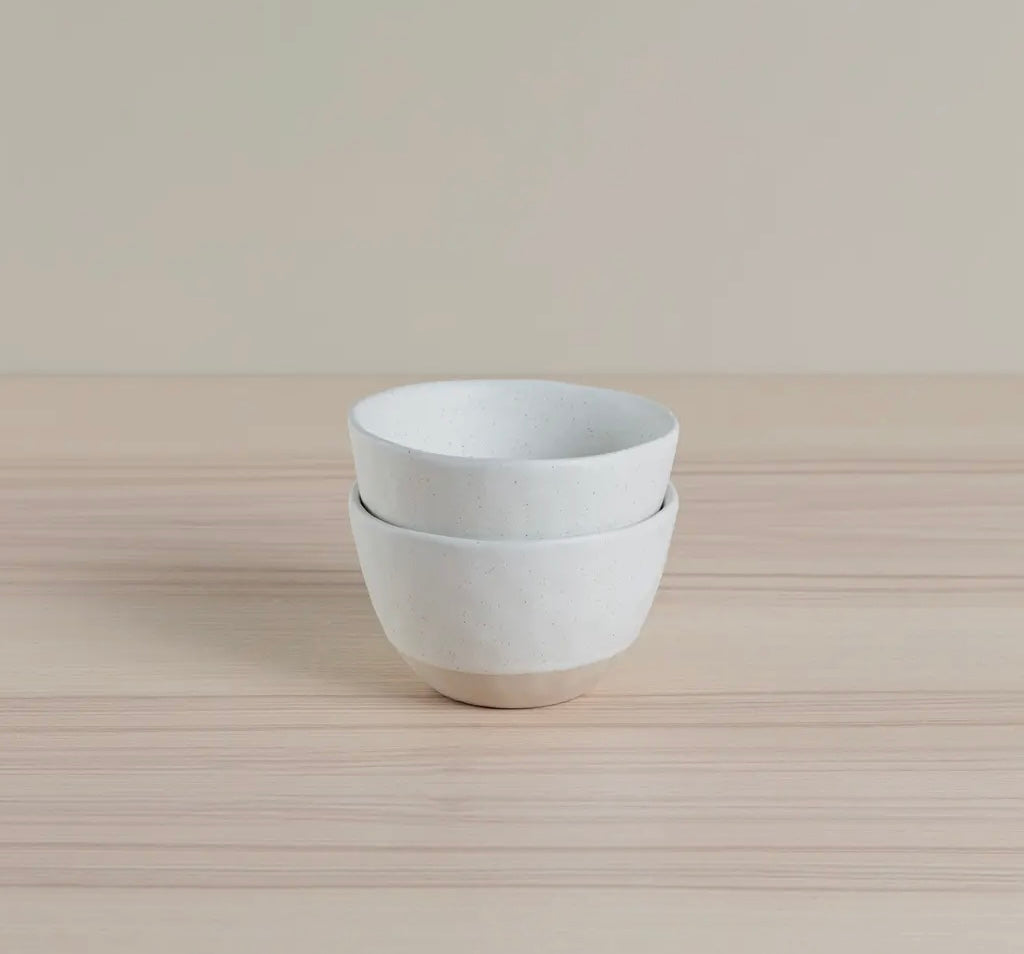 Stack of white Organics Nibbles Bowls on a light wooden surface with a neutral background