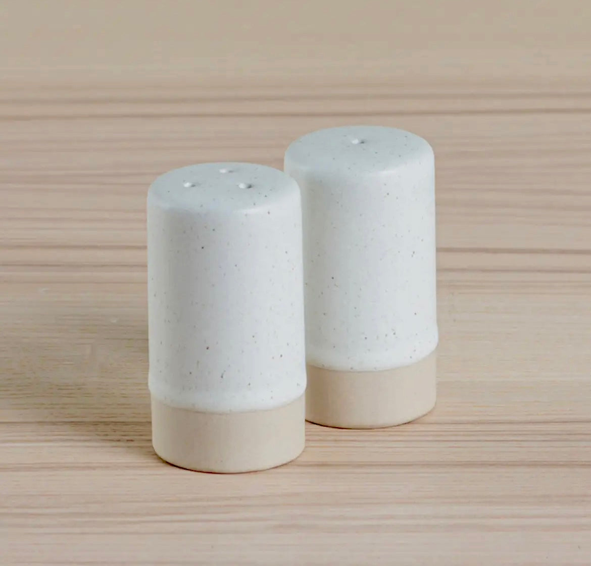 Two speckled ceramic salt and pepper shakers on a wooden surface