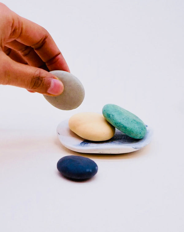 Hand placing a gray stone on a small plate with other stones, on a white background