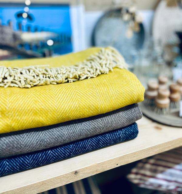 Stack of yellow, grey, and blue textured blankets on a wooden surface with a blurred background.