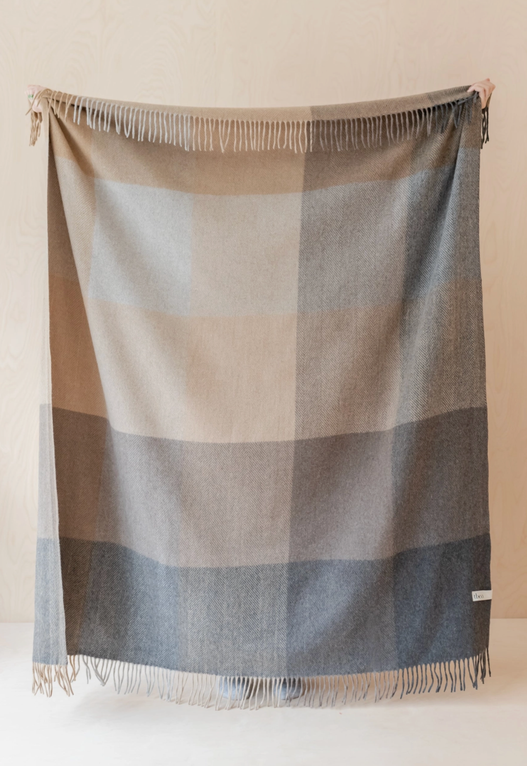 Checkered blanket with fringes draped over a surface against a beige background