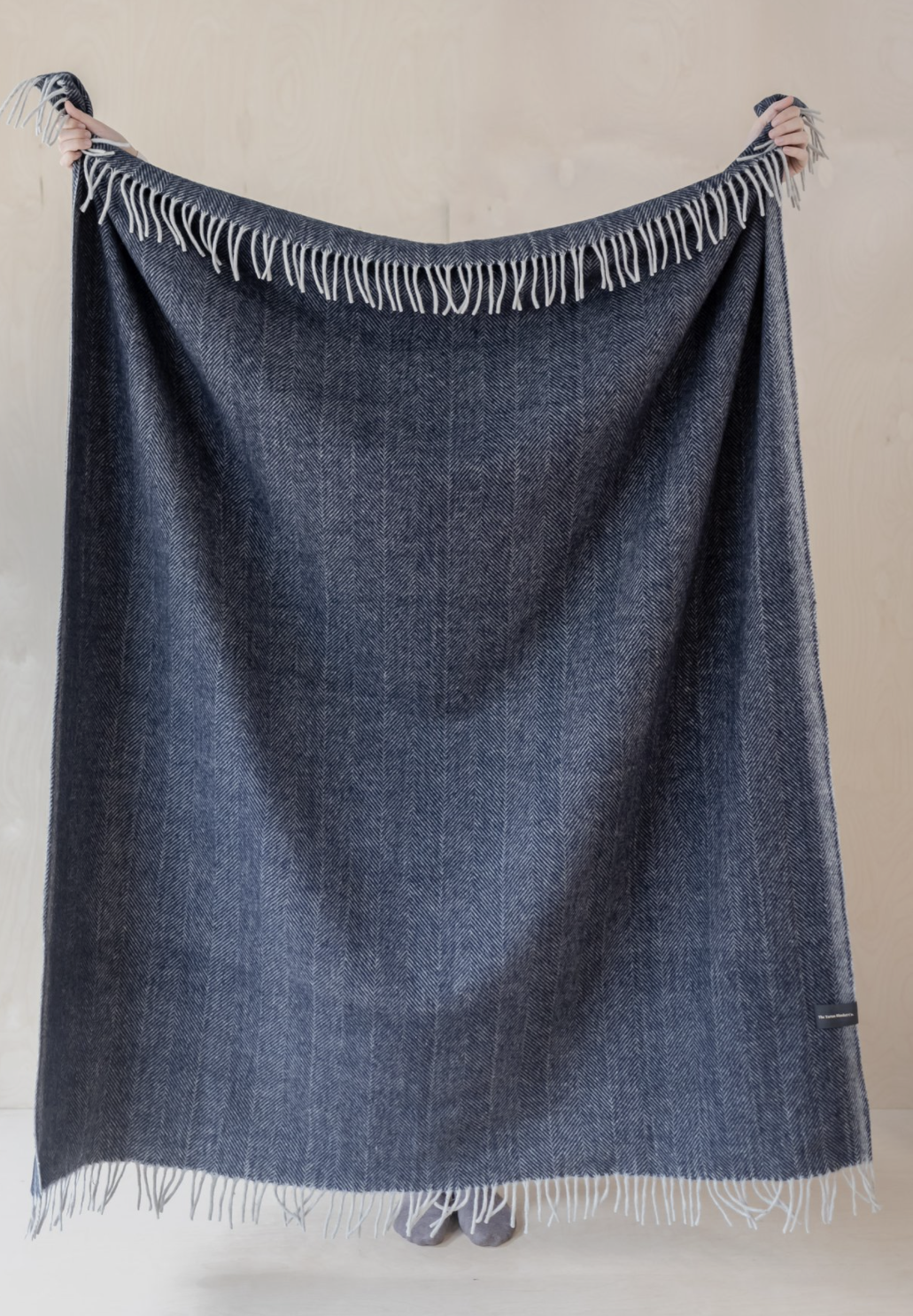 Blue blanket with fringes held up against a plain background