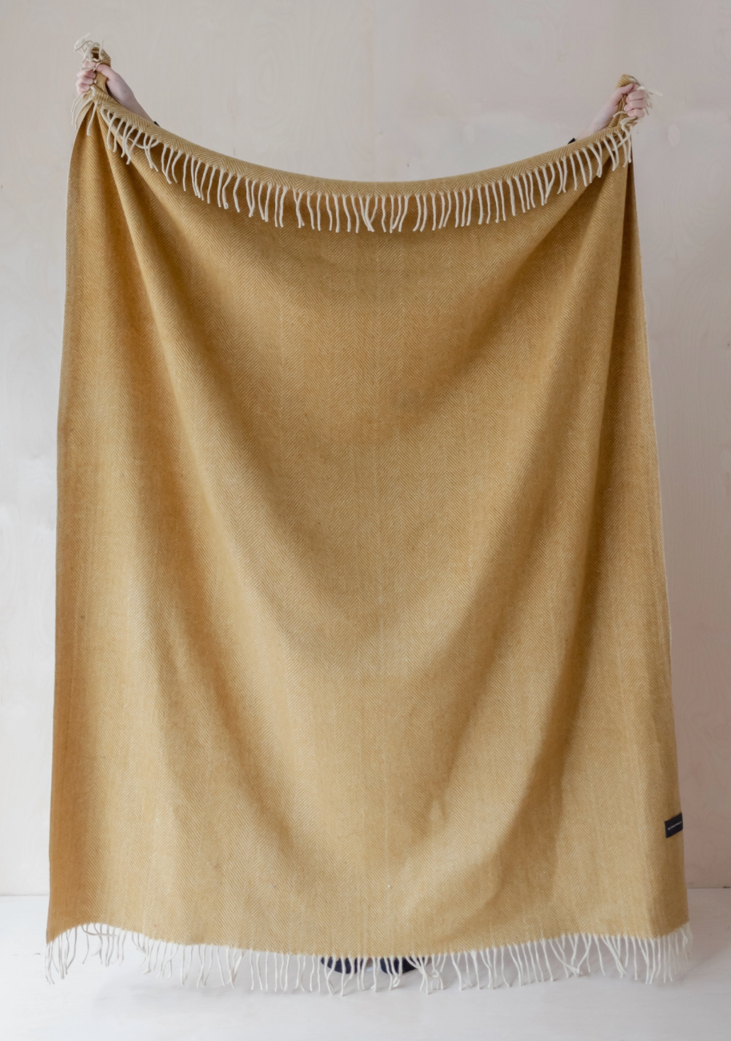 Beige throw blanket with white fringe on a plain background