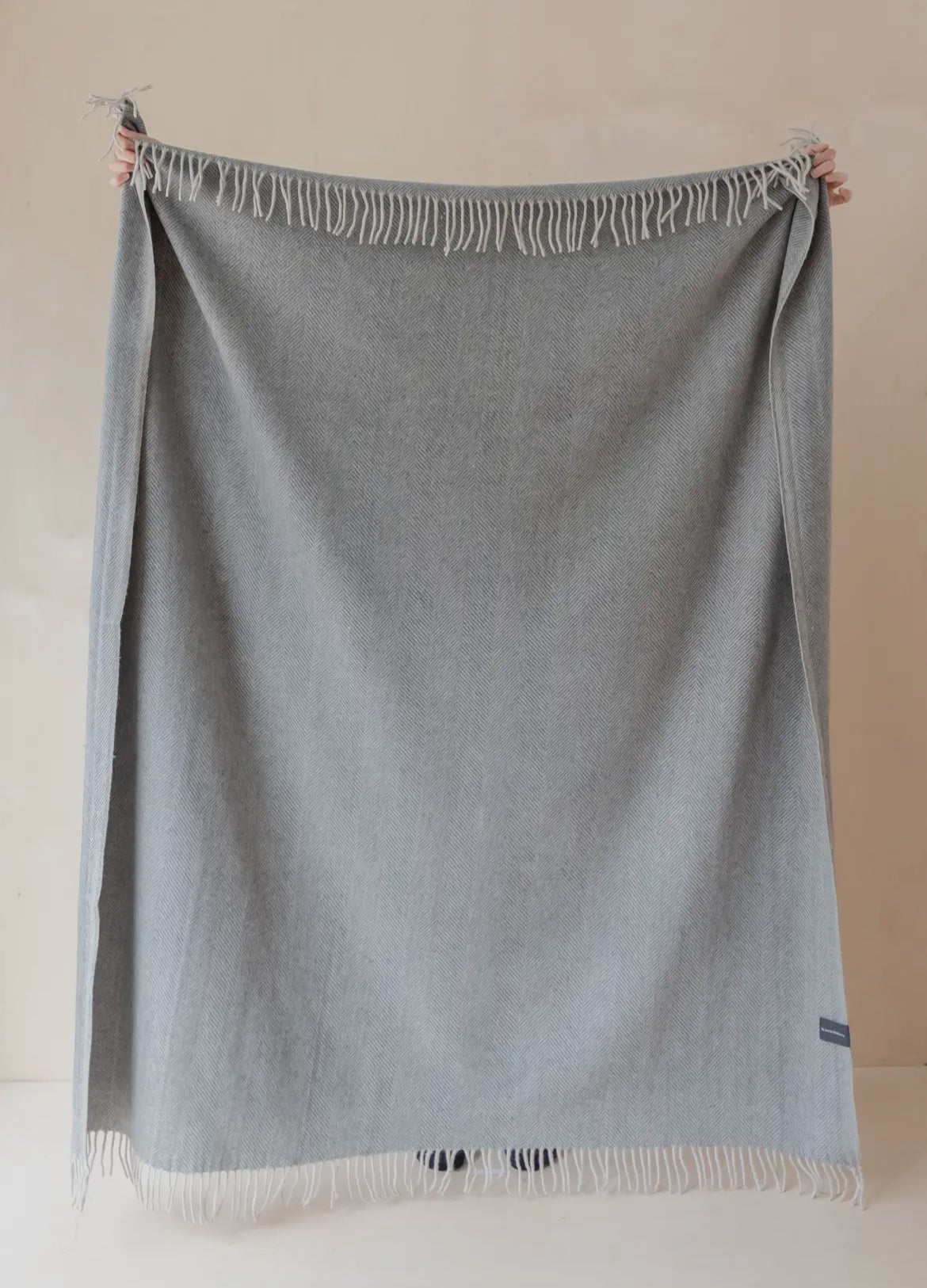 Gray blanket with white fringe held against a beige background