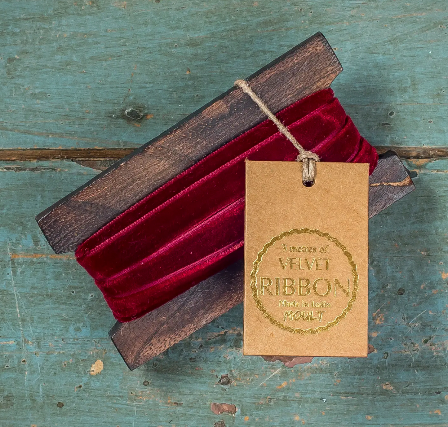 Red velvet ribbon in a wooden box with a 'Mores of Velvet Ribbon' tag on a rustic wooden surface.