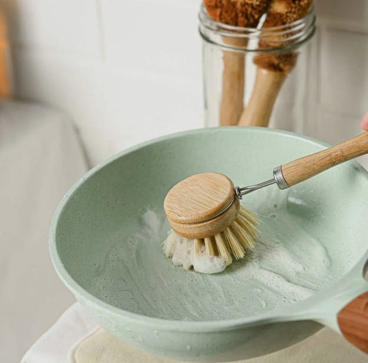 Dishwashing brush with wooden handle and natural bristles cleaning a green bowl.
